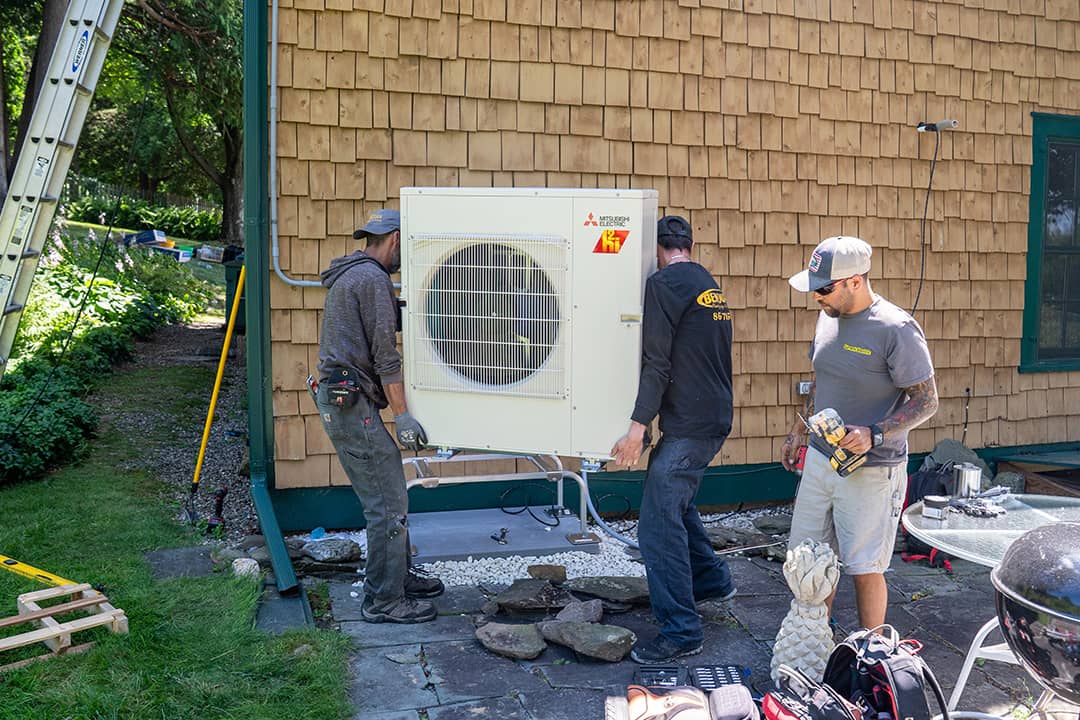 HVAC technicians prepare to install a condenser to a residential heat pump system.